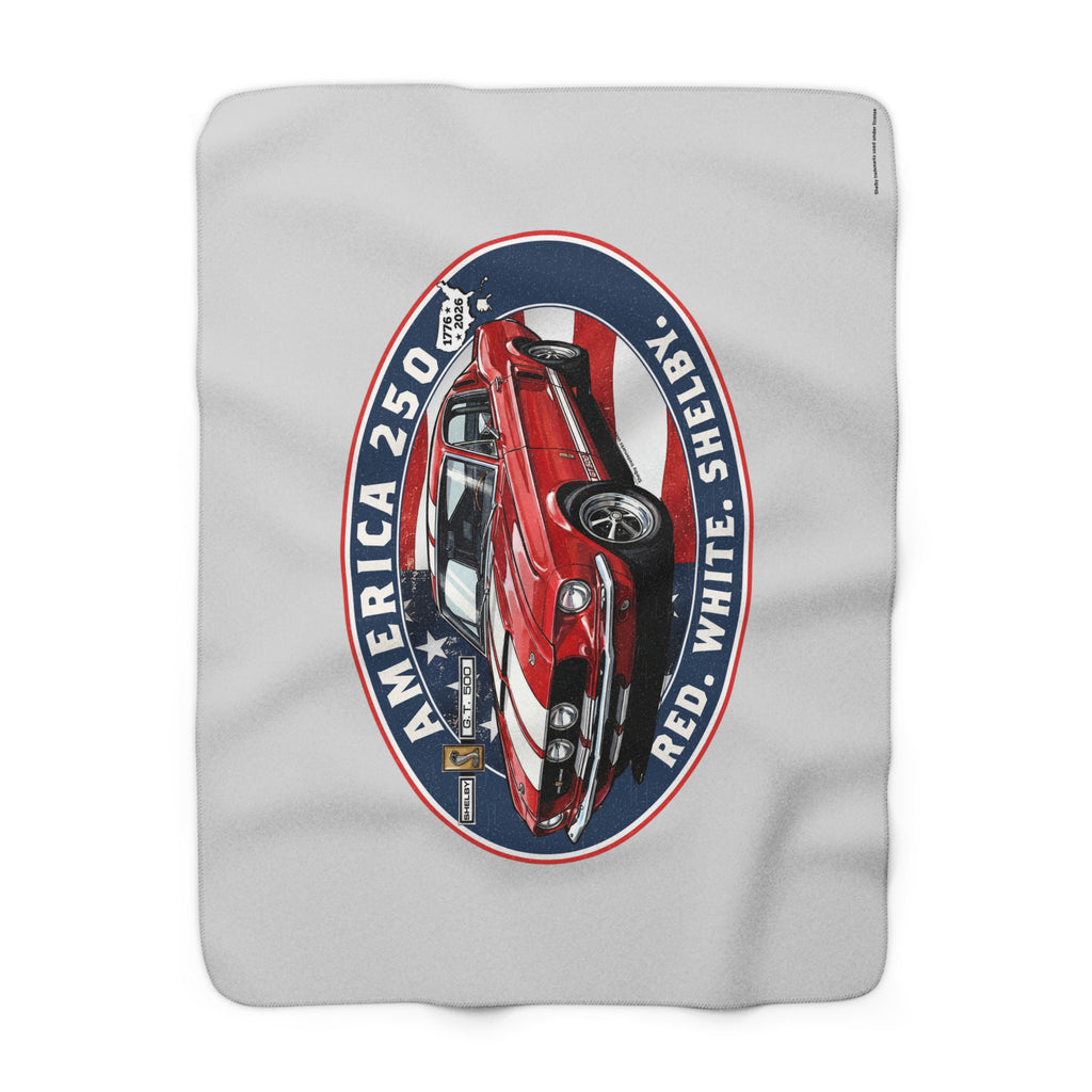 A light gray blanket featuring a large vintage-style oval graphic of a red, white, and blue classic car with the text 'AMERICA 250', 'SHELBY', and 'RED WHITE'.