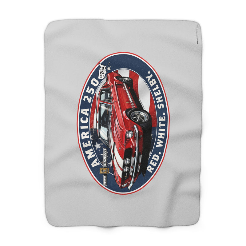 A light gray blanket featuring a large vintage-style oval graphic of a red, white, and blue classic car with the text 'AMERICA 250', 'SHELBY', and 'RED WHITE'.